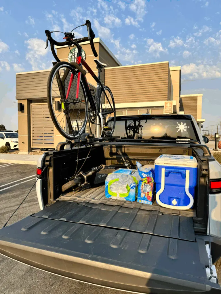 Rivian R1T with the bed open showing what's inside is an electric scooter, cooler, water, and rack with bicycle.