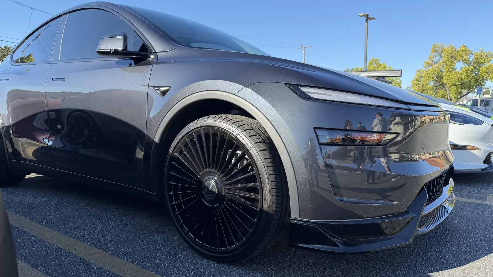 Tesla Model Y Juniper in Stealth Grey close-up, showing deep-dish multi-spoke black 22-inch wheels with low-profile staggered tires.