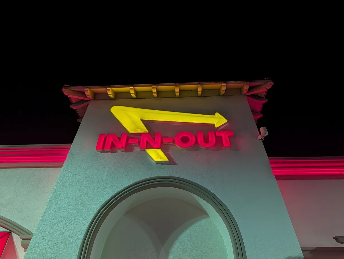 Bright red and yellow neon In-N-Out Burger sign glowing against a dark night sky