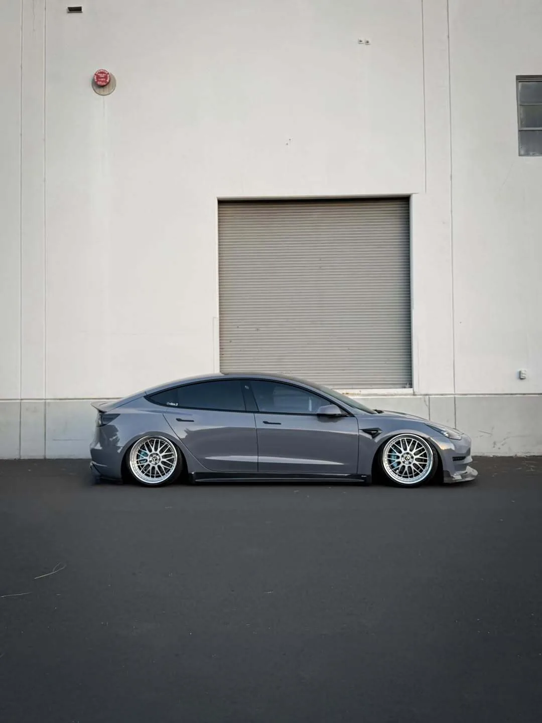 Profile view of Marvin's bagged Model 3 on Work wheels at full drop, gray with gold-flake wrap against a white building