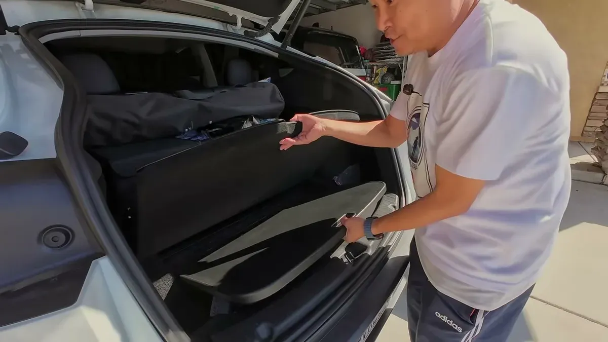 Man adjusting black portable foldable table in the open trunk of a white Tesla Model Y