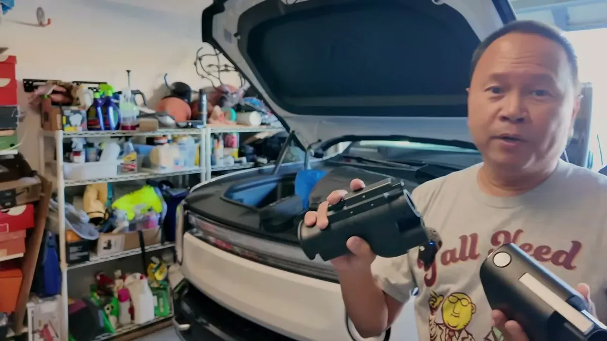 Man comparing two black EV charging adapters with open Rivian frunk.