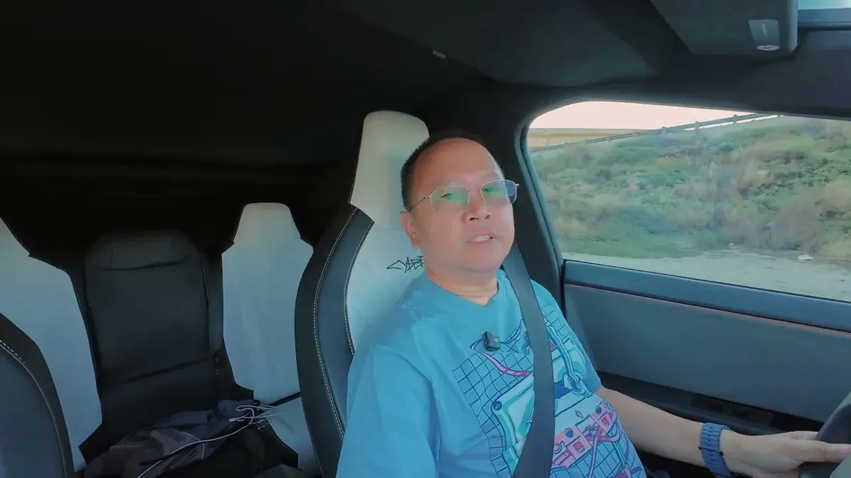 Man in light blue t-shirt in Cybertruck driver's seat talking to camera before leaving for service