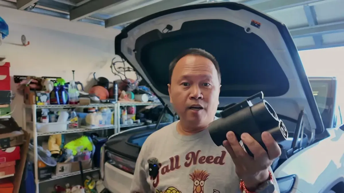 Man holding black EV charging adapter in front of open Rivian frunk.