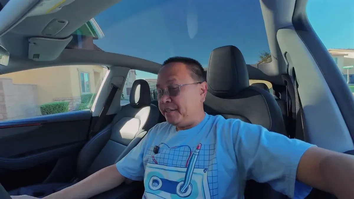 Man in light blue t-shirt in red Model Y Launch Series, panoramic roof visible
