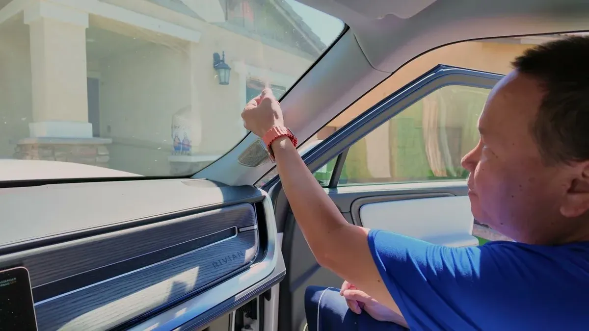 Man inside Rivian R1S reaching toward windshield area, Rivian dashboard logo visible.