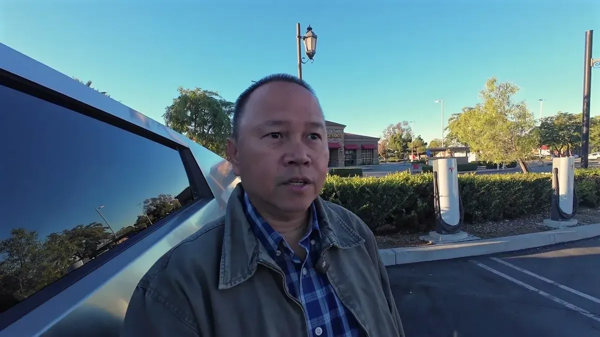 Man standing next to silver Tesla Cybertruck at Upland service center, clear blue sky