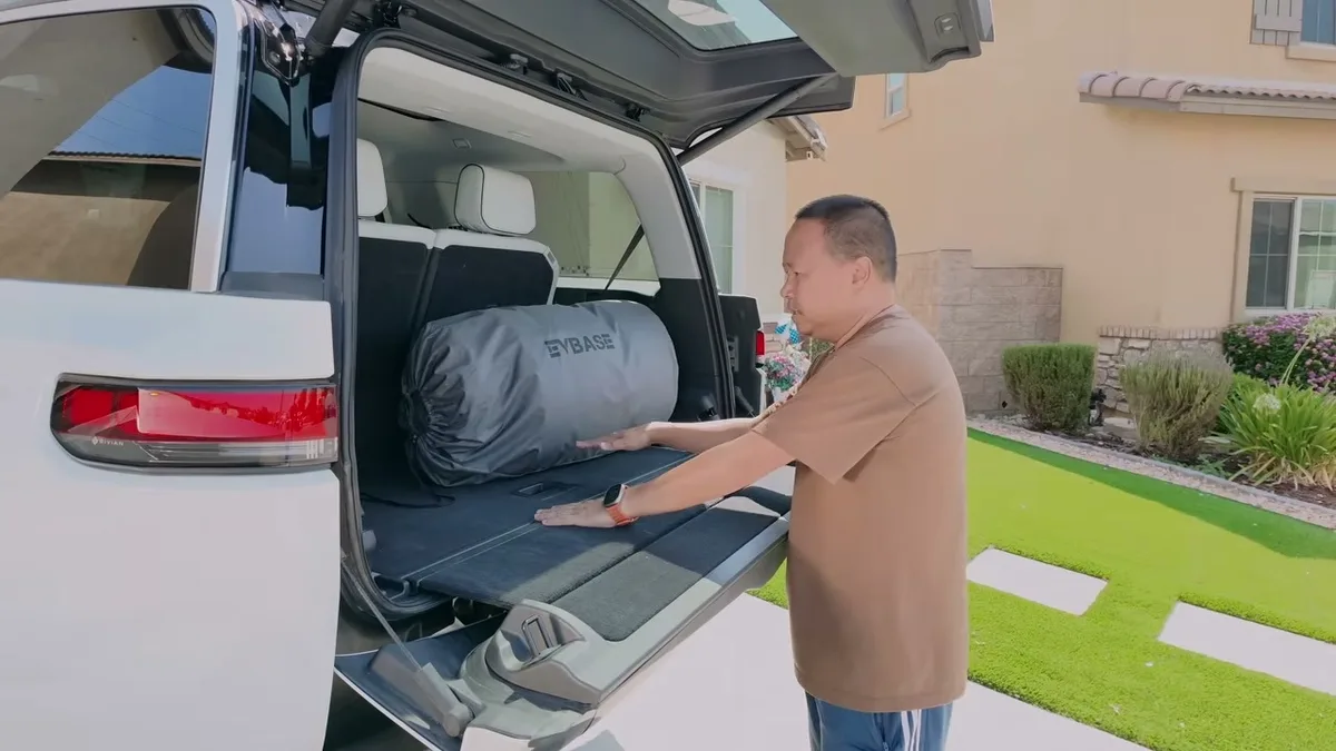 Sherwin placing the EVBase bag into the open trunk of a white Rivian R1S with the sub-trunk floor visible