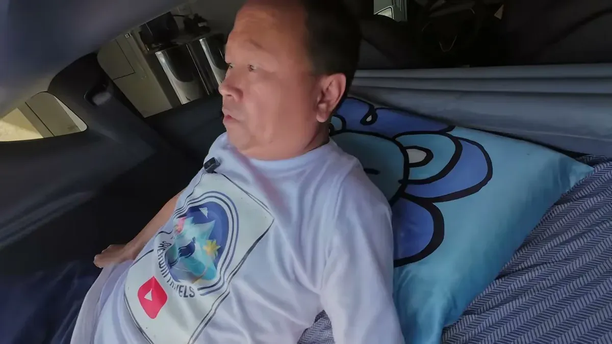 Man lying on inflated air mattress in Tesla Model Y trunk, head on blue pillow, looking relaxed