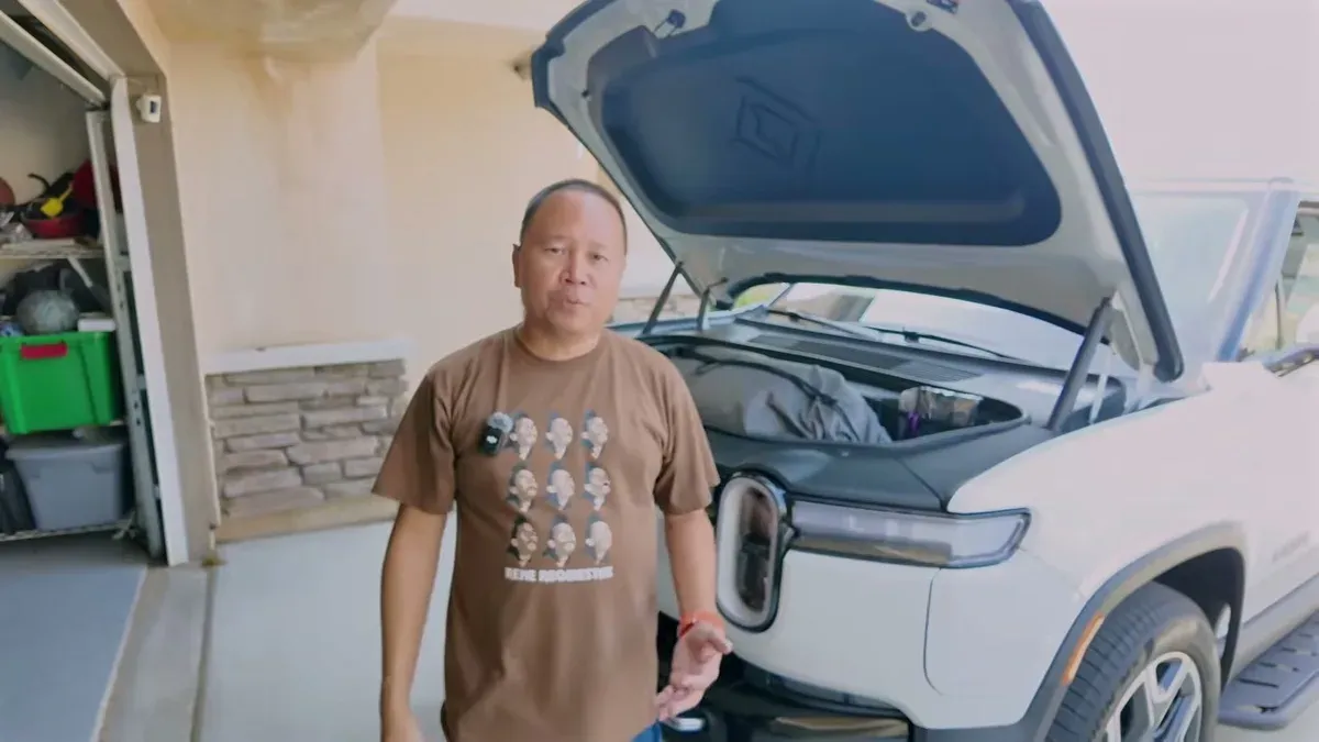 Sherwin standing in his garage next to a white Rivian R1S with the frunk open, holding the EVBase air mattress bag