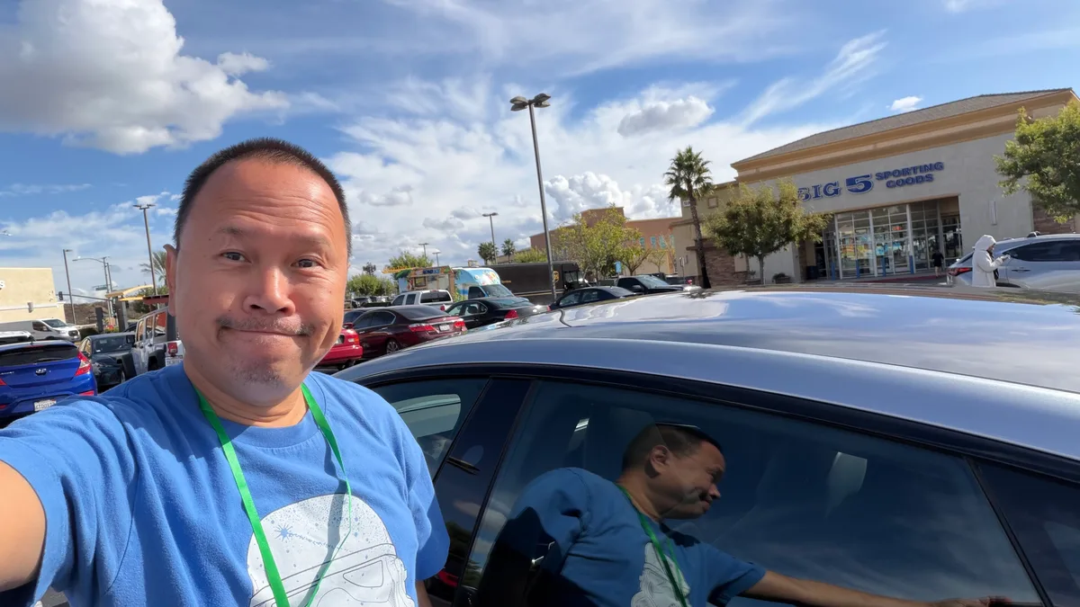 Man taking a selfie with the silver 2026 Tesla Model S in a parking lot.