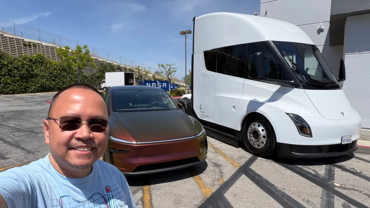 Man taking a selfie in front of a custom gold-wrapped Tesla Model Y and a white Tesla Semi at the Montebello grand opening.