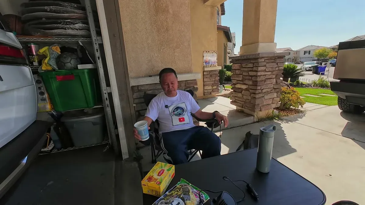 Man sitting in camping chair outside garage looking relaxed, white Tesla Model Y partially visible behind him