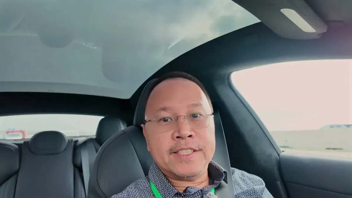 Man with glasses in driver's seat of a 2026 Tesla Model S, looking at camera with panoramic glass roof visible.