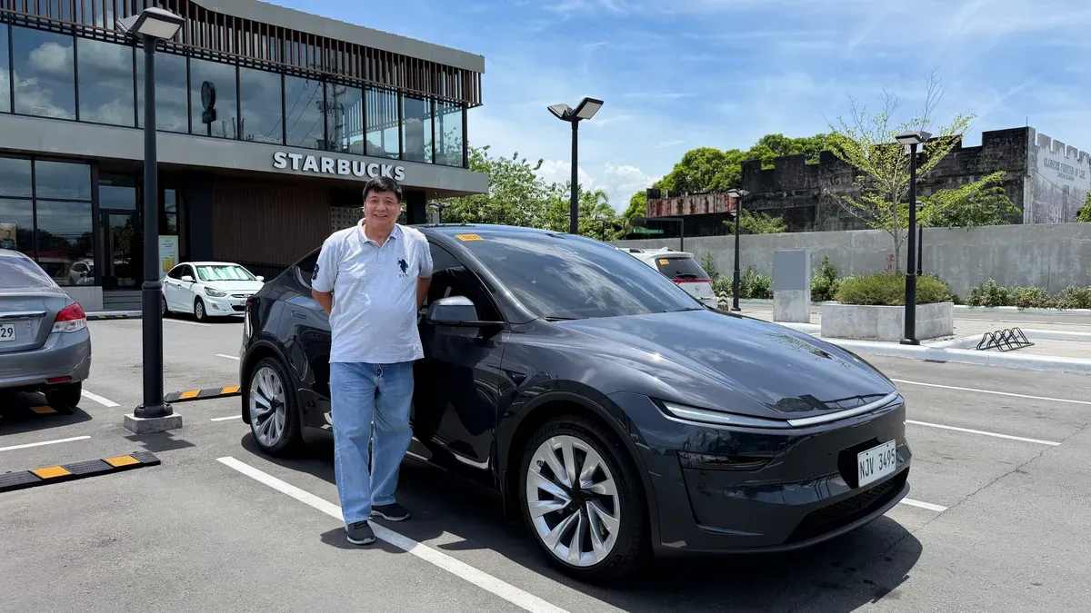 Doc Dennis standing next to his Stealth Gray Tesla Model Y in a Starbucks parking lot in Santa Cruz, Laguna
