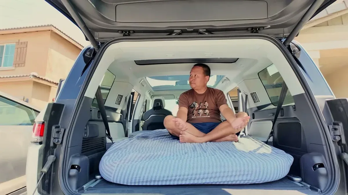 Sherwin sitting cross-legged on the inflated EVBase air mattress inside the open cargo area of a white Rivian R1S