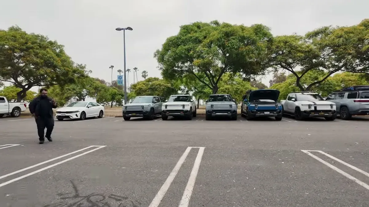 Man walking toward a lined-up row of Rivian R1T trucks at the event