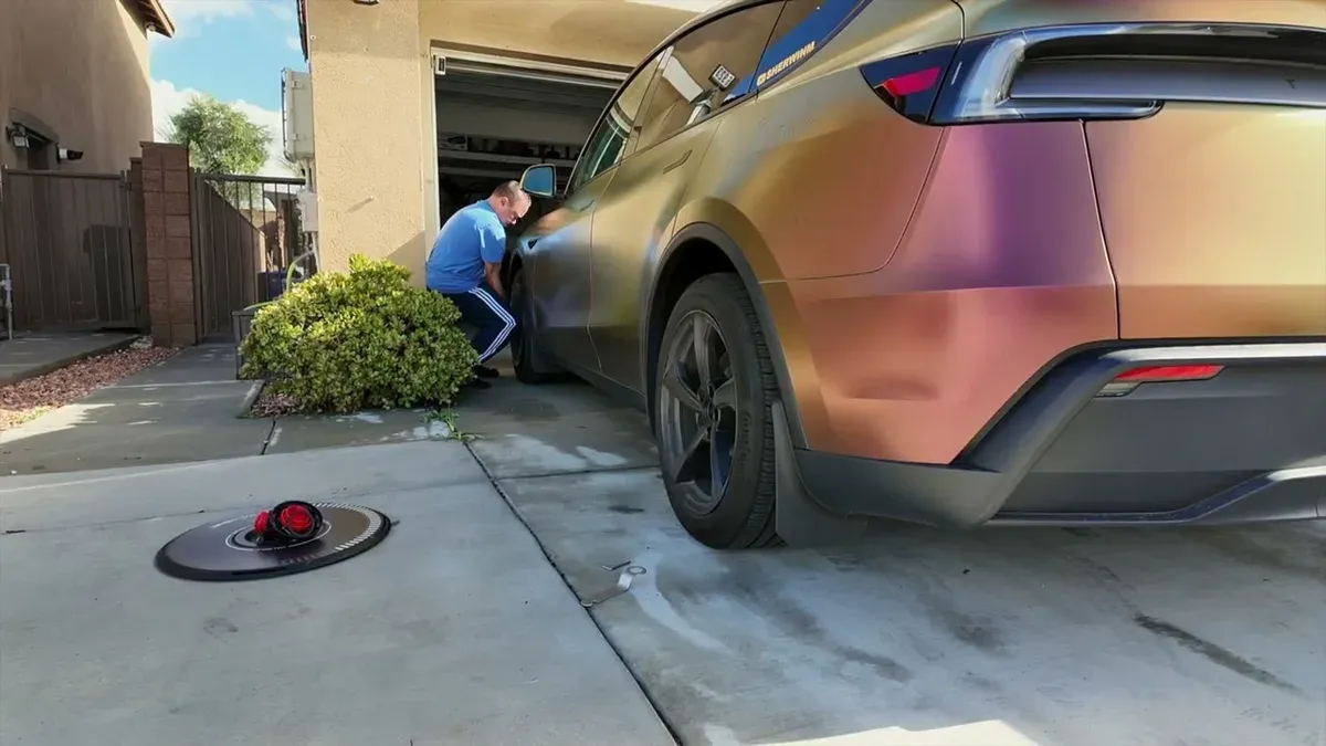 Man removing aftermarket wheel covers from the wrapped Model Y Juniper in the driveway before the service appointment.