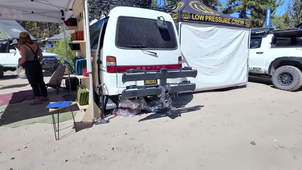 White Mitsubishi Delica 4x4 van at Toyo Trail Pass event with DELICA badge visible and vendor displays nearby