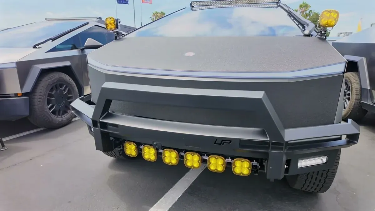 Front view of a modified matte black Tesla Cybertruck with yellow auxiliary lights and roof light bar at EV Fest 2026