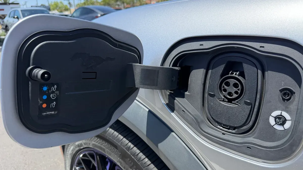 Open charging port on a silver Ford Mustang Mach-E showing the EV socket and Mustang logo inside