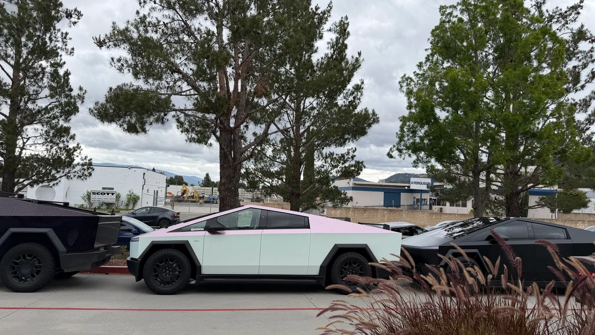 Side view of a white and pink custom Cybertruck between dark Cybertrucks.