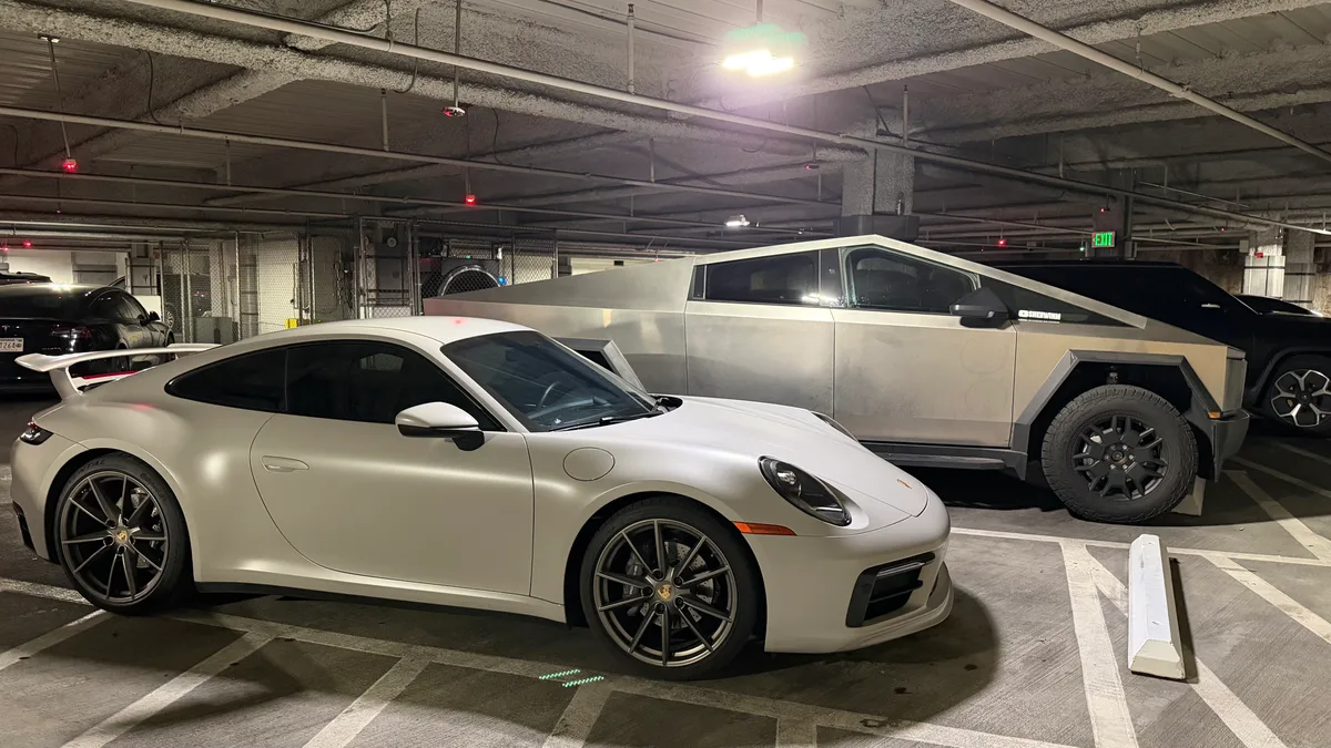 White Porsche 911 parked in front of Tesla Cybertruck in underground garage.