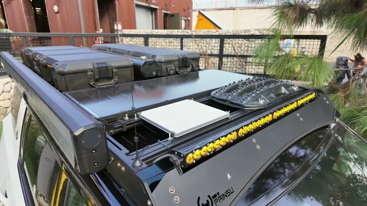 Overhead view of the Prinsu roof rack with two Pelican cases, 100W solar panel, and yellow BD LED light bar