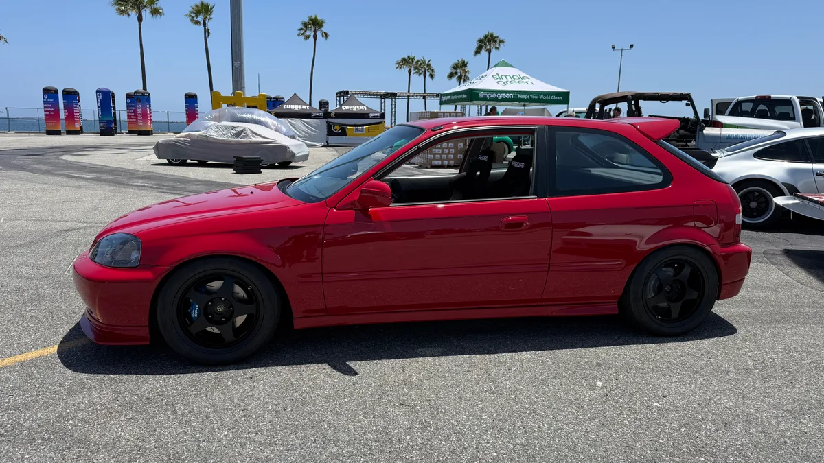 Red Honda Civic EK hatchback with black aftermarket wheels and rear spoiler at Electrify Expo