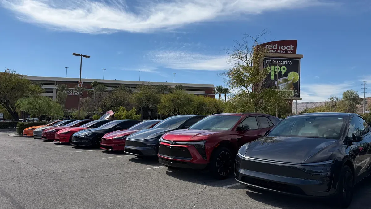 Long row of Teslas, a Chevy Blazer EV and Mach-Es parked nose to tail under the Red Rock Casino sign on a clear blue day in Las Vegas
