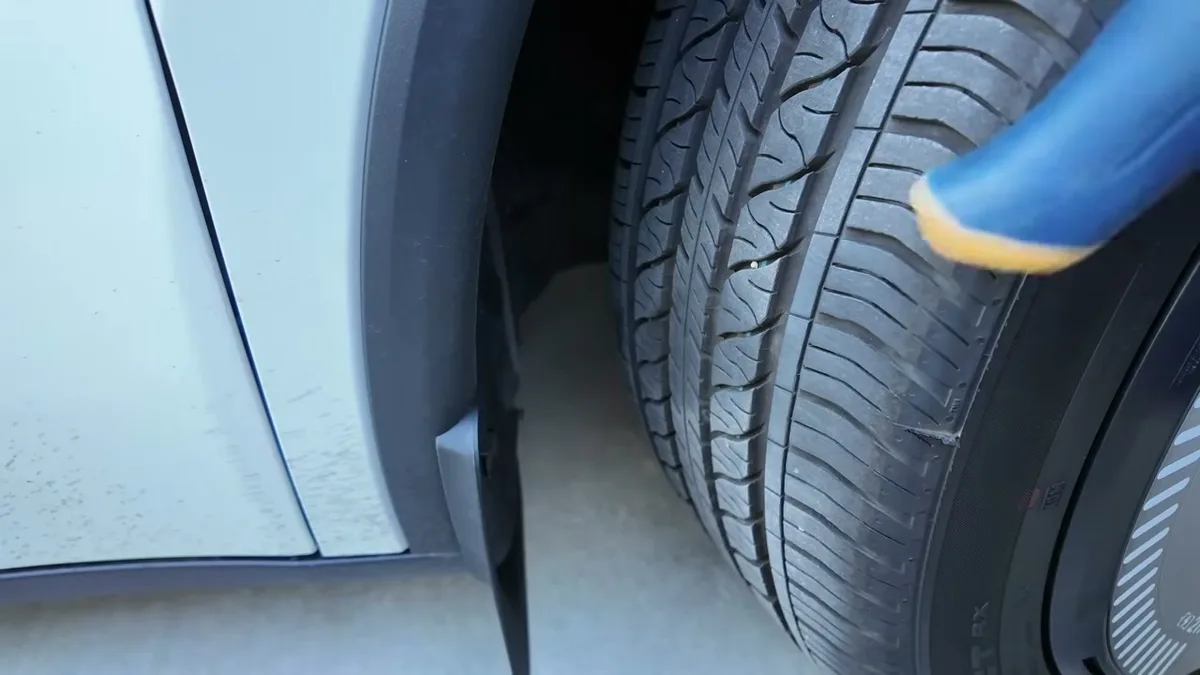 Blue tool prying open a push-pin fastener in a white Tesla's wheel well.