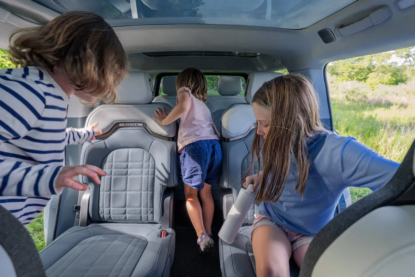 Two kids and an adult in the second row of a Rivian R1S, with a child walking through the center pass-through toward the third row