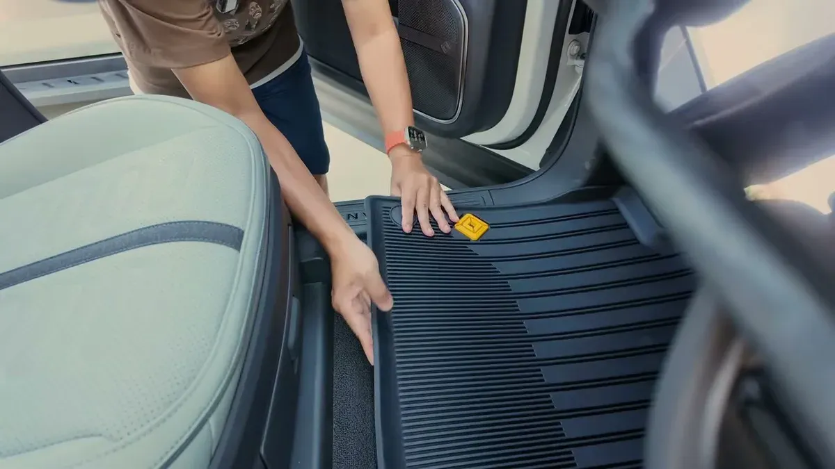 Man carefully positioning black Rivian all-weather floor mat into the driver's footwell