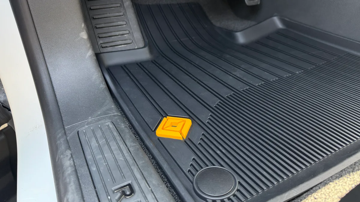 Installed Rivian floor mat showing R1 door sill branding and full driver footwell coverage