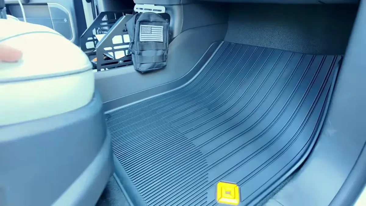 Rivian all-weather floor mat installed in front passenger footwell showing orange logo and full coverage