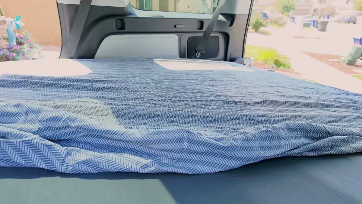 Blue and white patterned bed sheet draped over the EVBase inflatable mattress inside the Rivian R1S