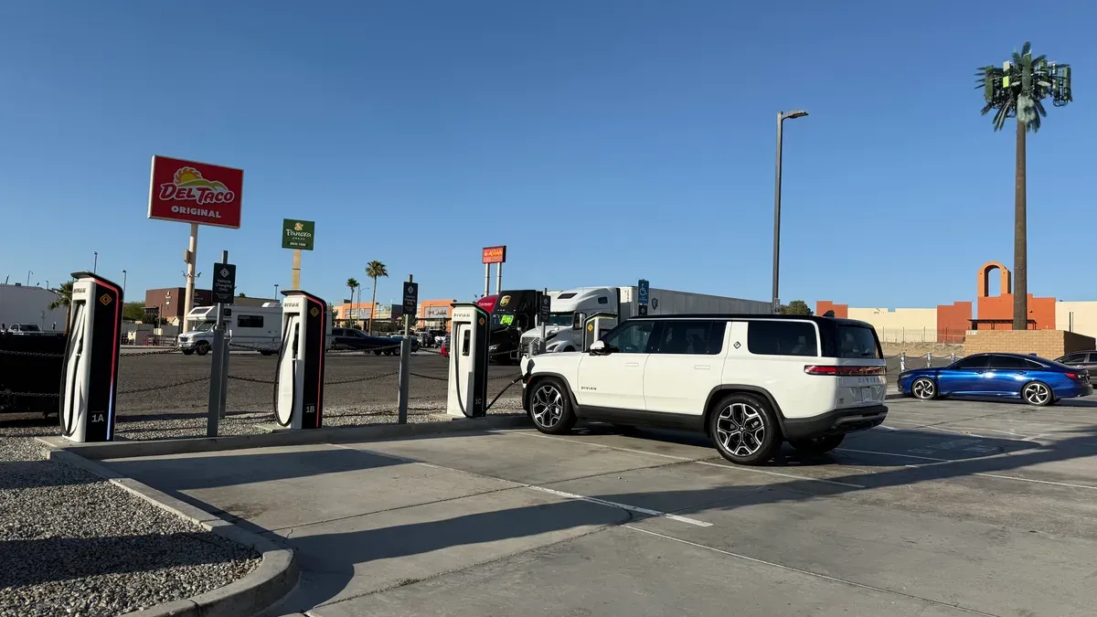 White Rivian R1S charging at the Barstow Rivian Adventure Network in a sunny parking lot