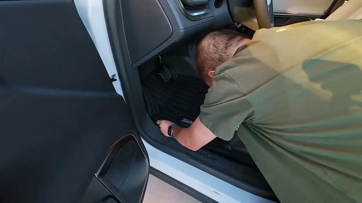 Man installing black 3W floor mat on the driver's side of a white Rivian R1S
