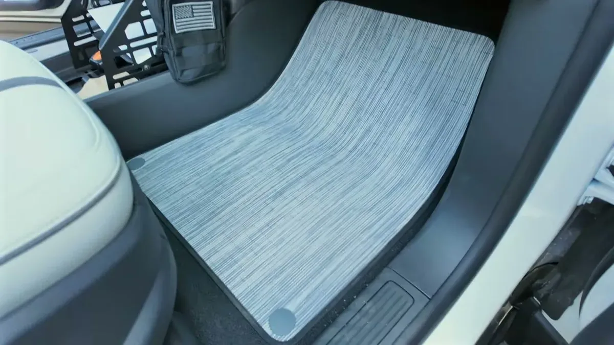 Light gray striped factory floor mat in Rivian R1S driver's footwell with white seat visible