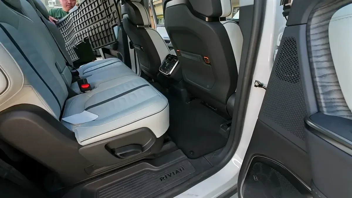 Man preparing to place large black 3W second-row floor mat inside white Rivian R1S