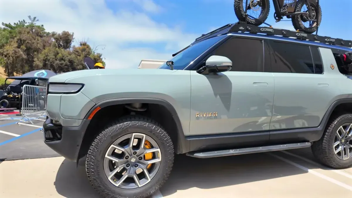 Light gray Rivian R1S SUV with off-road tires, orange calipers, and a Super73 electric bike on its roof rack.