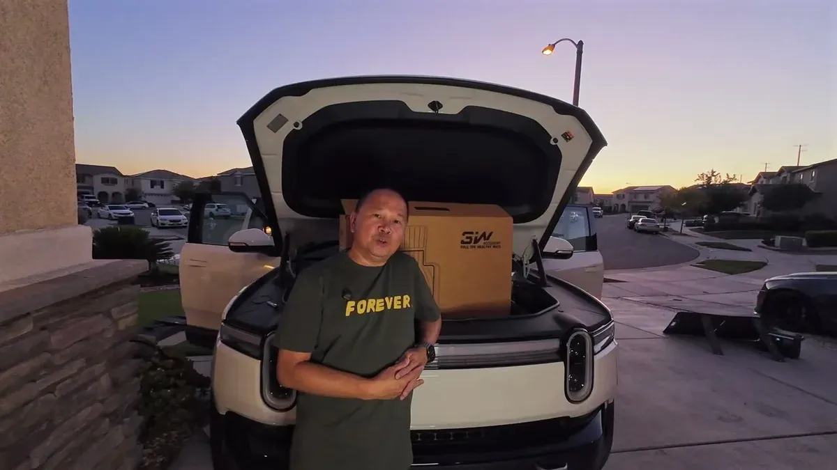 Man standing in front of white Rivian R1S with frunk open and 3W floor mat box visible at sunset