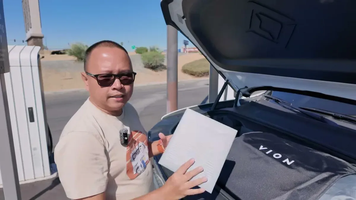 Holding Vion cabin air filter box in front of open R1S frunk at charging station