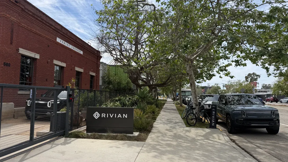 Rivian R2 SUV parked next to a Rivian sign in front of the Venice Postal building.
