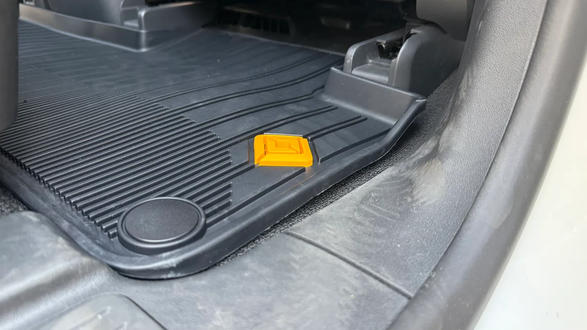 Close-up of black Rivian all-weather floor mat with yellow logo in driver's footwell