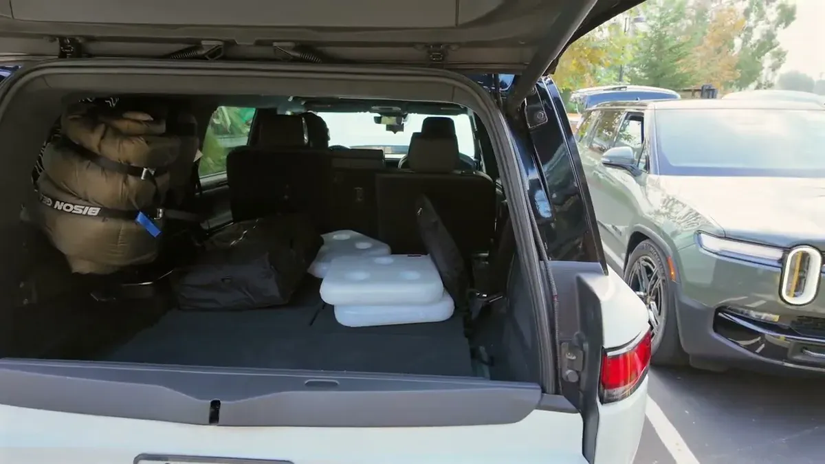 Open tailgate of white Rivian R1S showing cargo area with a large Bison sleeping bag and white coolers inside