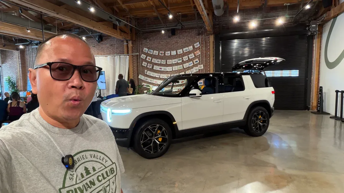 Sherwin in a San Gabriel Valley Rivian Club shirt with a white Rivian R2, rear liftgate open, inside the Rivian Pasadena space