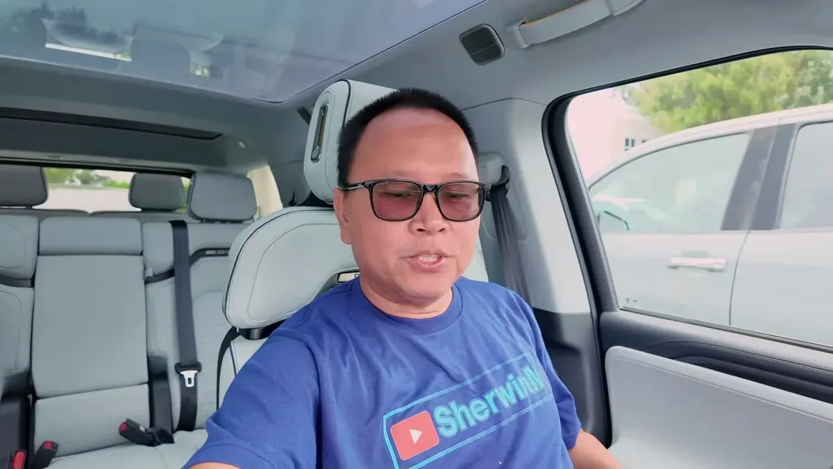 Man in SherwinM t-shirt in driver's seat of a light gray Rivian R1S with panoramic roof.