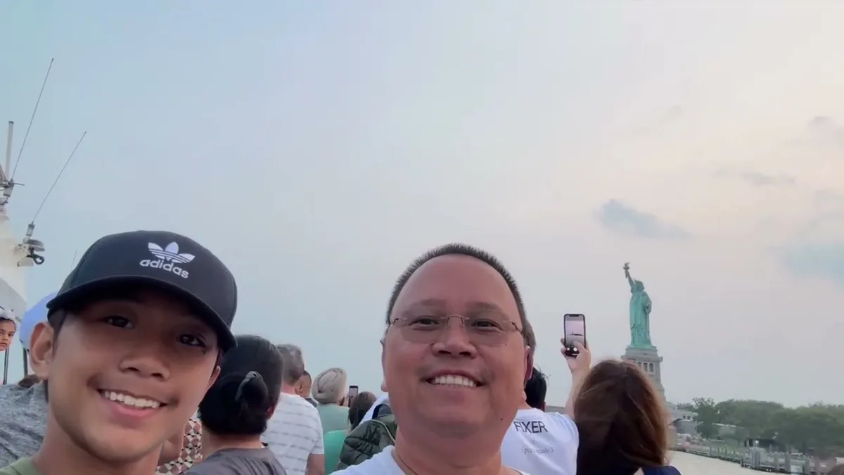 Sherwin and his son taking a selfie on a boat with the Statue of Liberty in the background