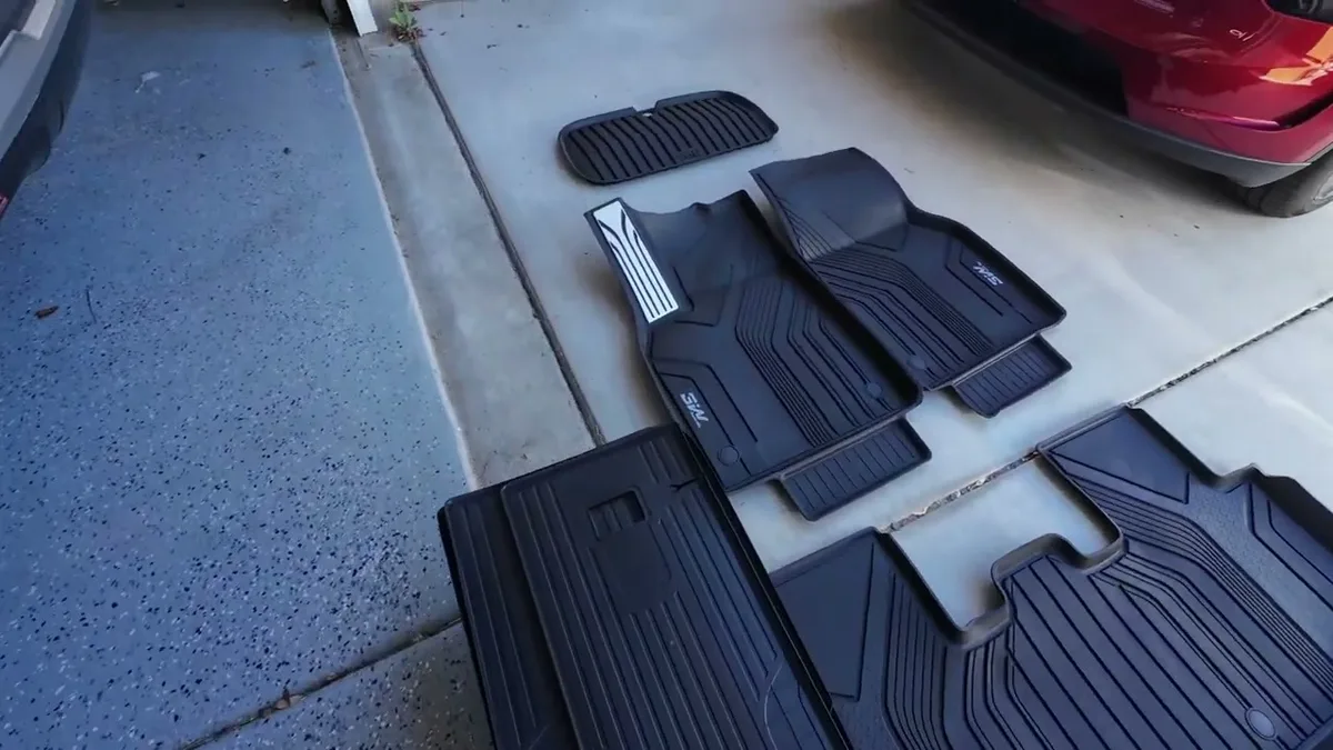 Black 3W custom-fit floor mats for Tesla Model Y laid out on a concrete driveway